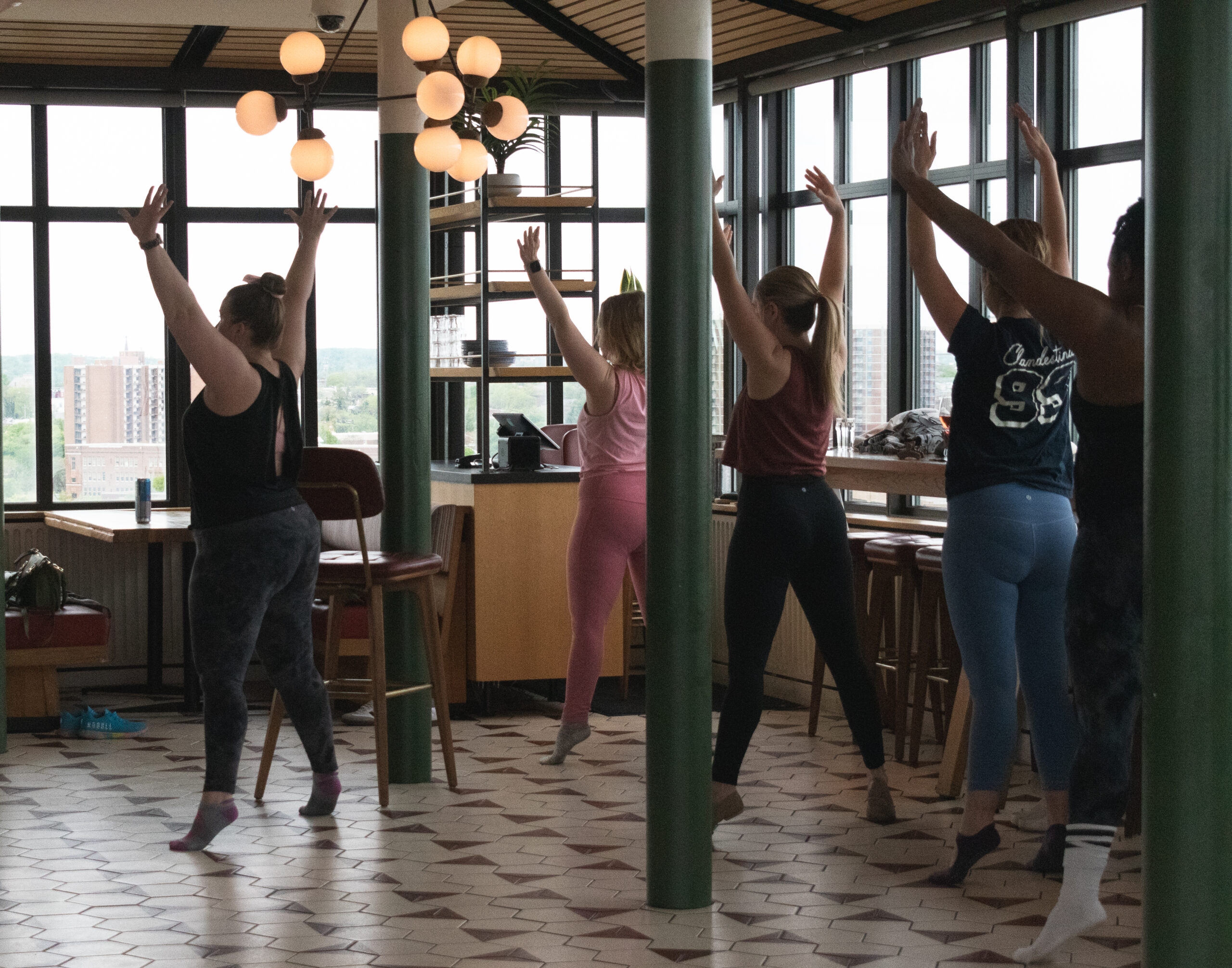 Group fitness class with participants doing stretching exercises in bright studio with pendant lights.