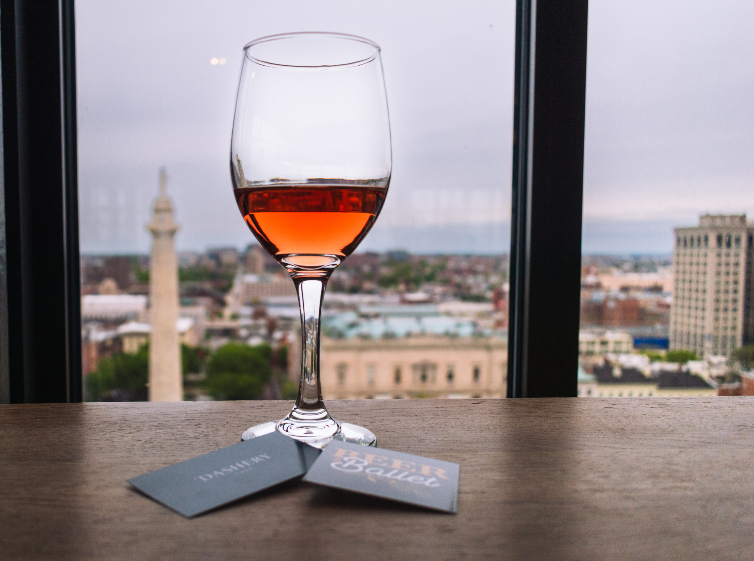 Glass of rosé wine on table overlooking cityscape with historic monuments and blue-tinted buildings.