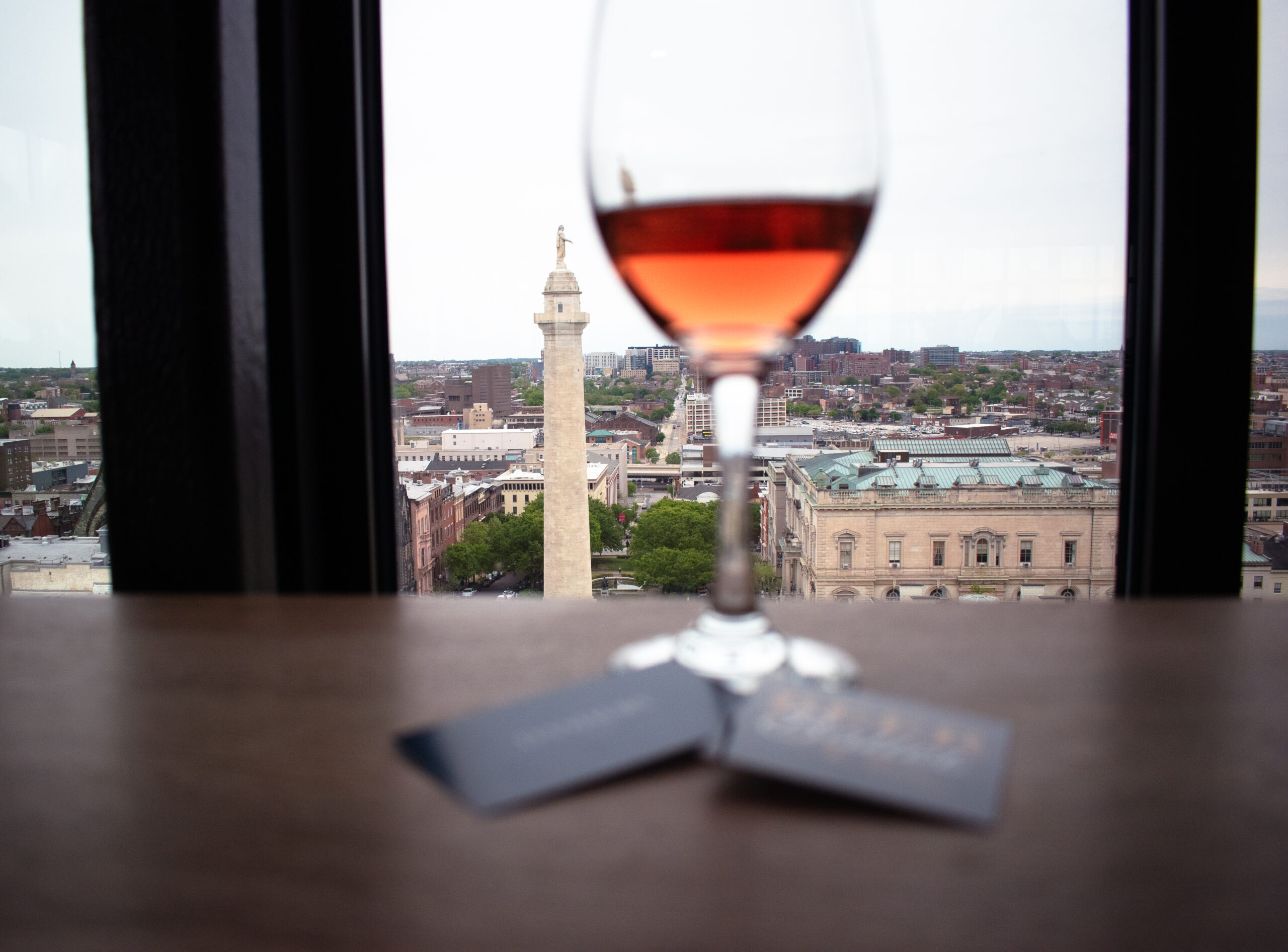 Wine glass with red wine on table framing cityscape view with historic landmarks and buildings.